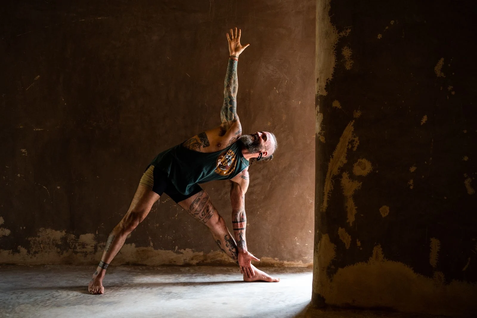 Ashton practicing a standing yoga posture with one arm extended upward in a sunlit room.
