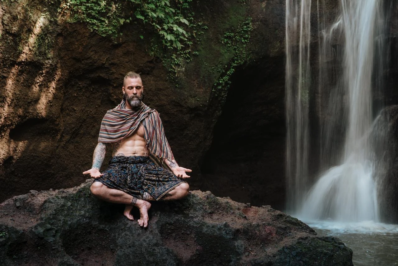 Ashton seated in meditation on a rock beside a waterfall.